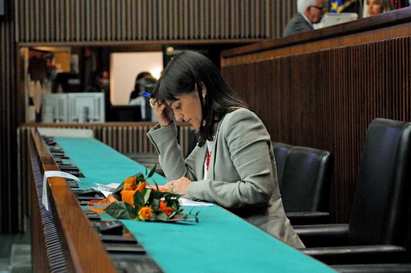 Debora Serracchiani seduta presso l'aula del Consiglio regionale del Friuli Venezia Giulia affiancata da un mazzo di fiori-narrazione